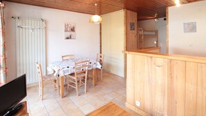 A cozy room with a wooden ceiling, a dining table with chairs, a TV, and a radiator.
