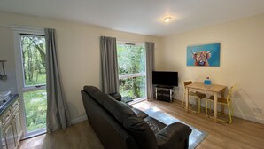 A living room with a sofa, a TV, a dining table with chairs, and a painting on the wall.