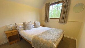 A neatly made bed with a quilt, a bedside table with a lamp, and a window with curtains.