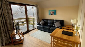 A living room with a black leather sofa, a wooden coffee table, a laptop, and a view of a snowy landscape through a glass door.