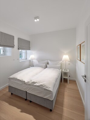 Un dormitorio con cama, lámparas de noche, una ventana con persianas y una puerta.