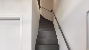 A modern staircase with dark steps and metal handrails, leading to a landing with a light fixture. - Gästehaus Cantzheim I Ferienwohnung Ritterpfad - Cantzheim.dorf (Kanzem)