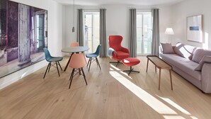 A modern living room with a round table, two chairs, a red armchair, a sofa, and a large abstract painting on the wall. - Gästehaus Cantzheim I Ferienwohnung Ritterpfad - Cantzheim.dorf (Kanzem)