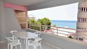 Un balcon avec une table ronde et quatre chaises, donnant sur une zone côtière avec des bâtiments et des arbres.
