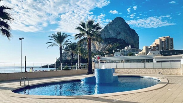 Une piscine avec une fontaine, des palmiers et une montagne rocheuse en arrière-plan.