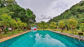 A swimming pool with a tiled surface, surrounded by lush greenery and a small building with a red door. - Ingthara Resort (Phang Nga)