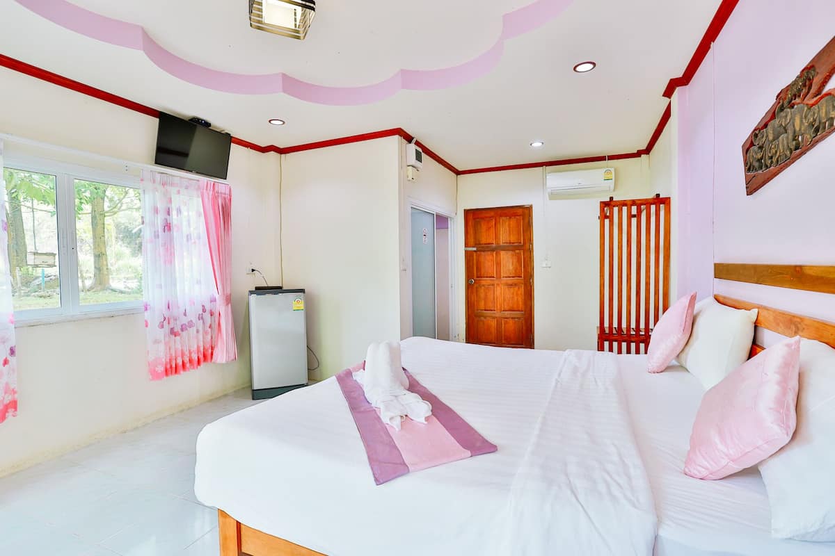 A hotel room with a bed, a window with curtains, a door, and a wall-mounted air conditioning unit.