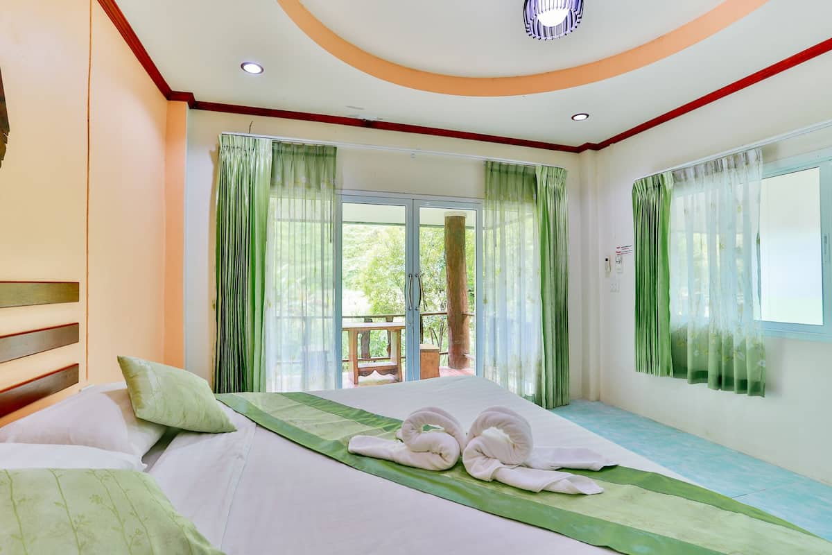 A hotel room with a bed, green curtains, a wooden headboard, and a view of the outdoors.