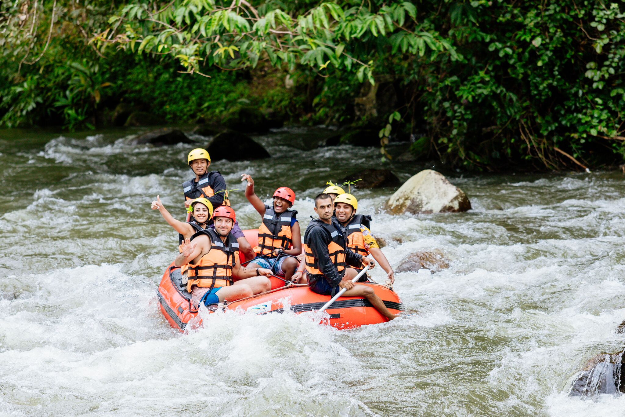 A group of people in an orange raft navigating a river surrounded by greenery.