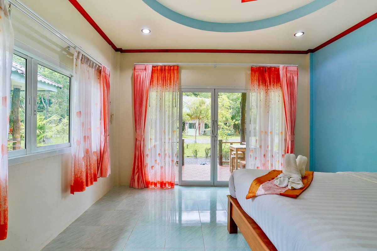 A bedroom with a bed, curtains, and a view of the outdoors.