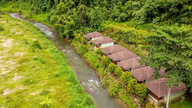 A row of traditional-style buildings with tiled roofs, situated beside a flowing river, surrounded by lush greenery. - Ingthara Resort (Phang Nga)
