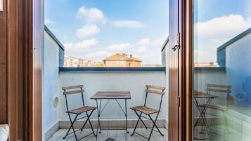 A balcony with a table and two chairs, a view of buildings in the background, and a clear sky.
