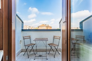 A balcony with a table and two chairs, a view of buildings in the background, and a clear sky.