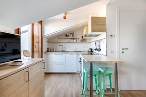 A modern kitchen with white cabinets, a wooden countertop, and a bar area with green stools.