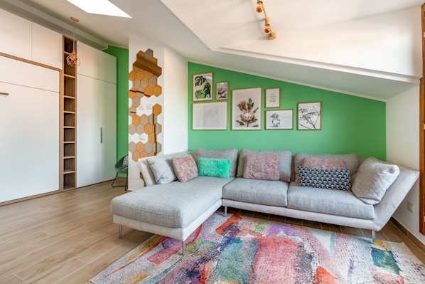 Un salon moderne avec un canapé d’angle, un tapis coloré et des œuvres d’art accrochées au mur.