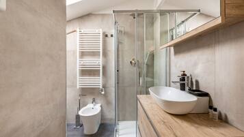 A modern bathroom with a glass-enclosed shower, a bidet, a large sink, and a wooden vanity.