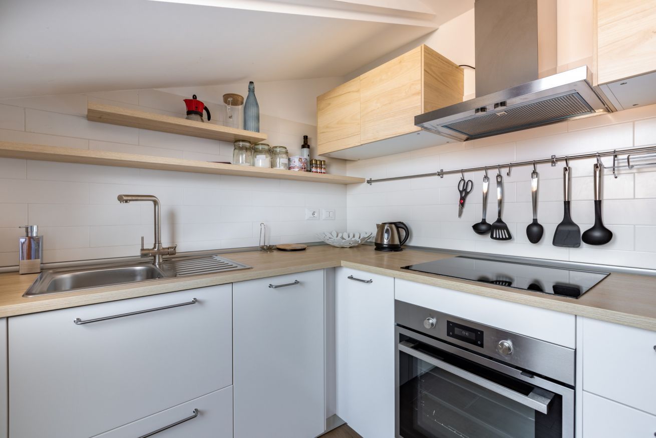 A modern kitchen with white cabinets, stainless steel appliances, wooden countertops, and a variety of utensils hanging on the wall.