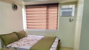 A small bedroom with a bed, a window with blinds, a wall clock, and a thermostat. - Avida Aspira Condotel (Cagayan de Oro)