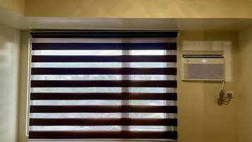 A room with horizontal blinds, a wall-mounted air conditioner, and a visible power outlet.