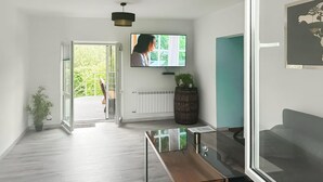 A modern living room with a glass coffee table, a television mounted on the wall, a potted plant, and a view of the outdoors through a sliding glass door. - Pet friendly home in Warnoleka with WiFi (Warnoleka)