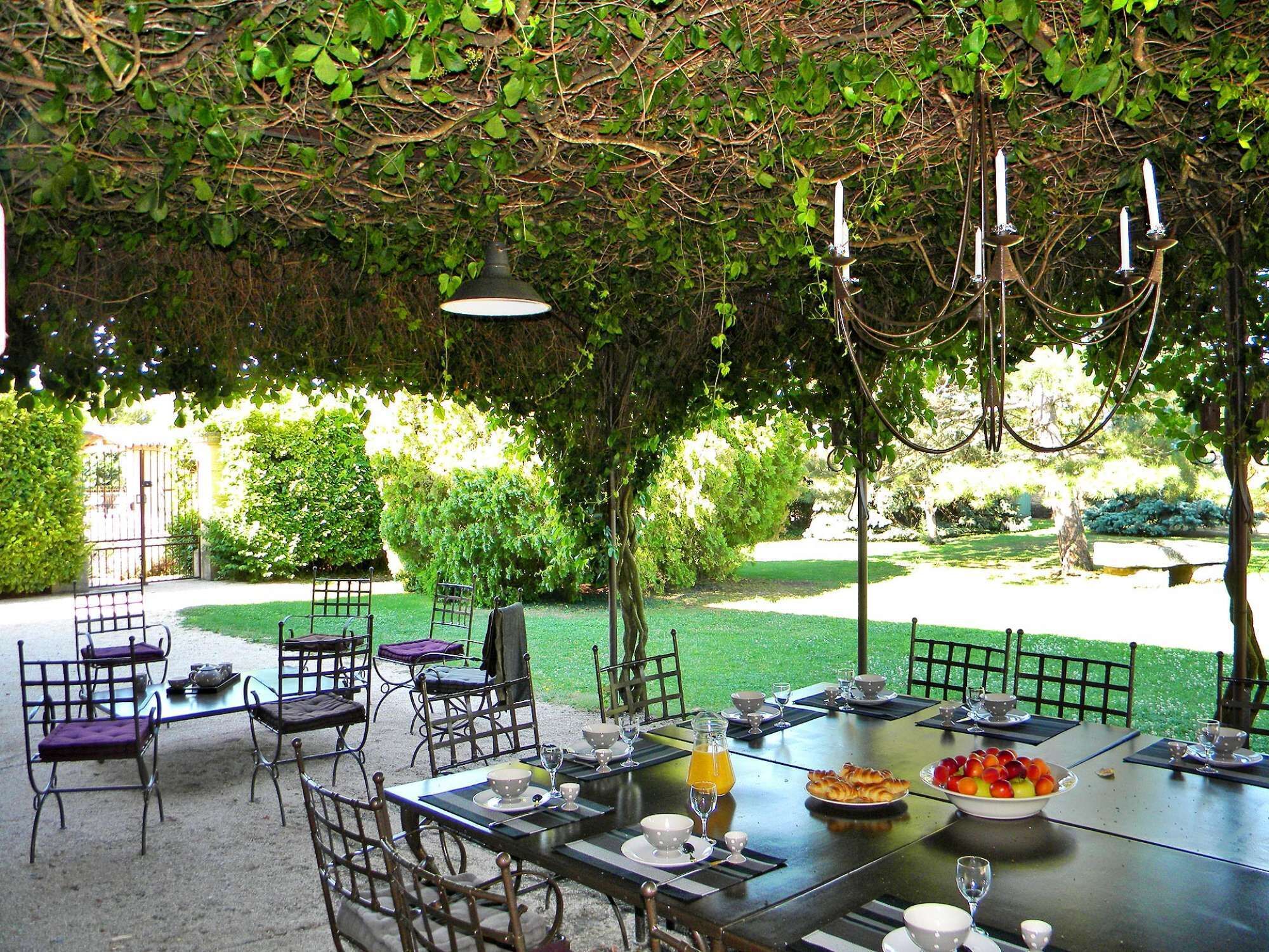 Un espace de restauration en plein air, avec des tables et des chaises, entouré de verdure et offrant une vue sur un jardin.