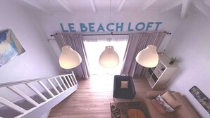 Ett modernt vardagsrum med en trappa, en soffa och en skylt med texten ”LE BEACH LOFT”.