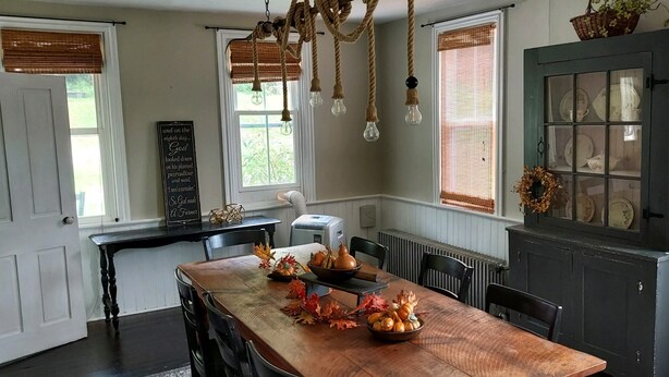 A dining area with a wooden table set for two, a dark cabinet with glass doors, and a window with a view of greenery.