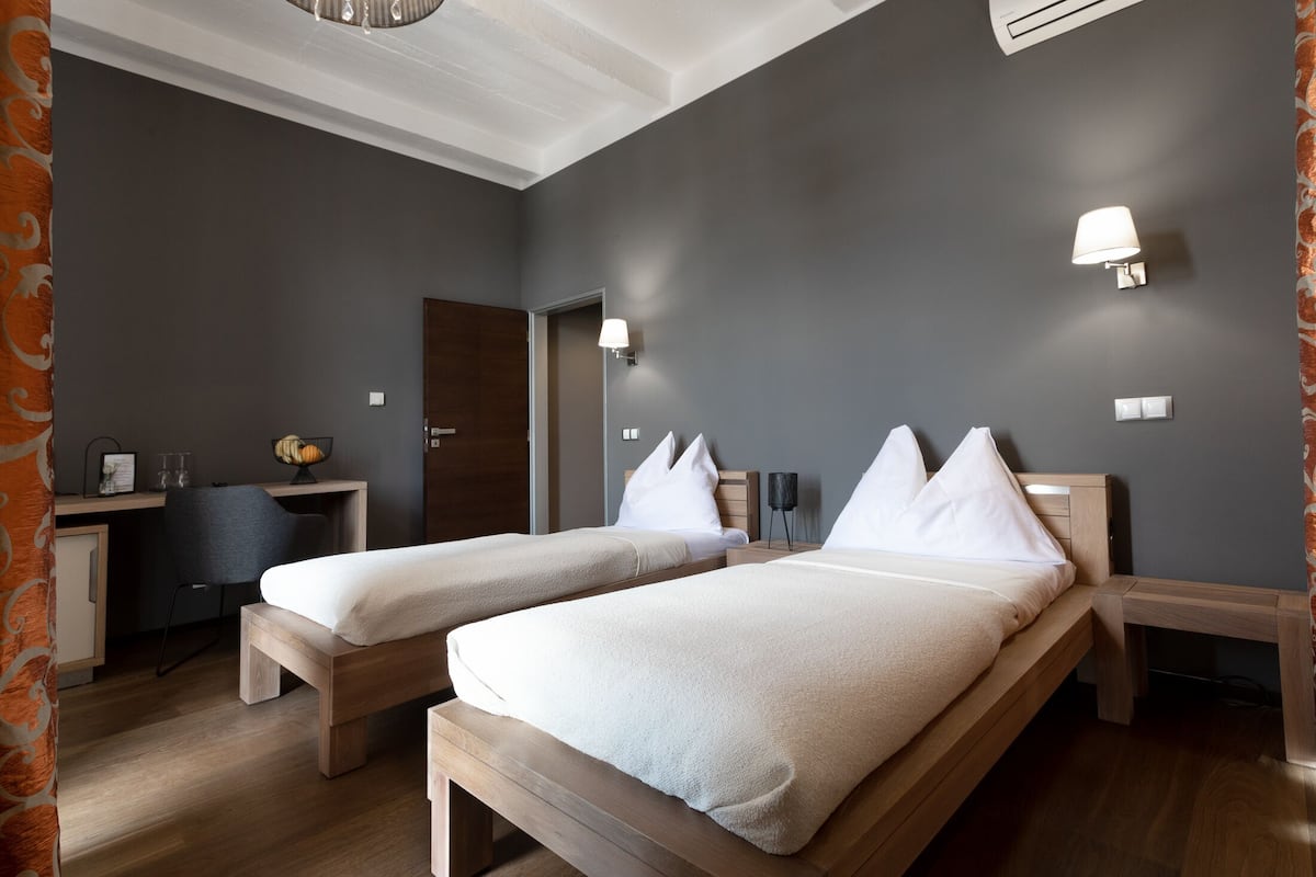 Quarto de hotel com duas camas de solteiro, uma mesa e uma cadeira.