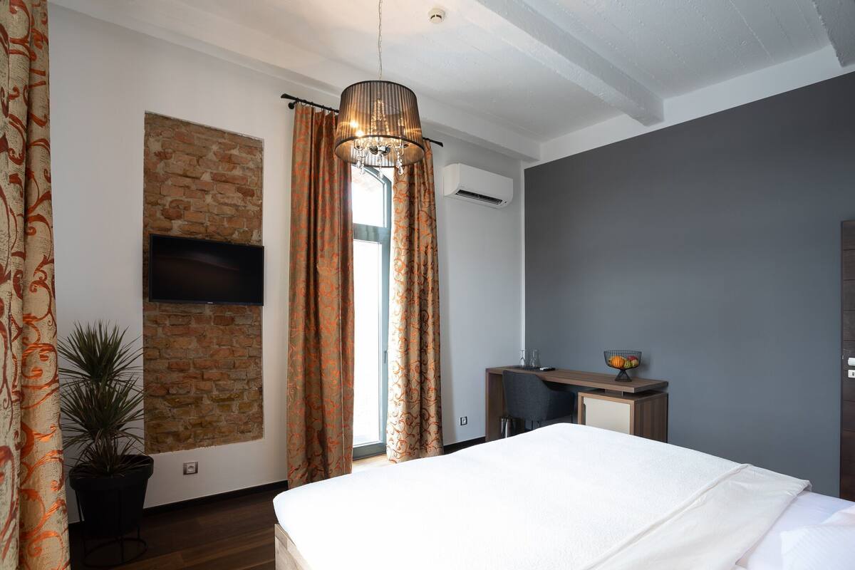 Quarto com cama, escrivaninha, planta em vaso, televisão e parede de tijolos.