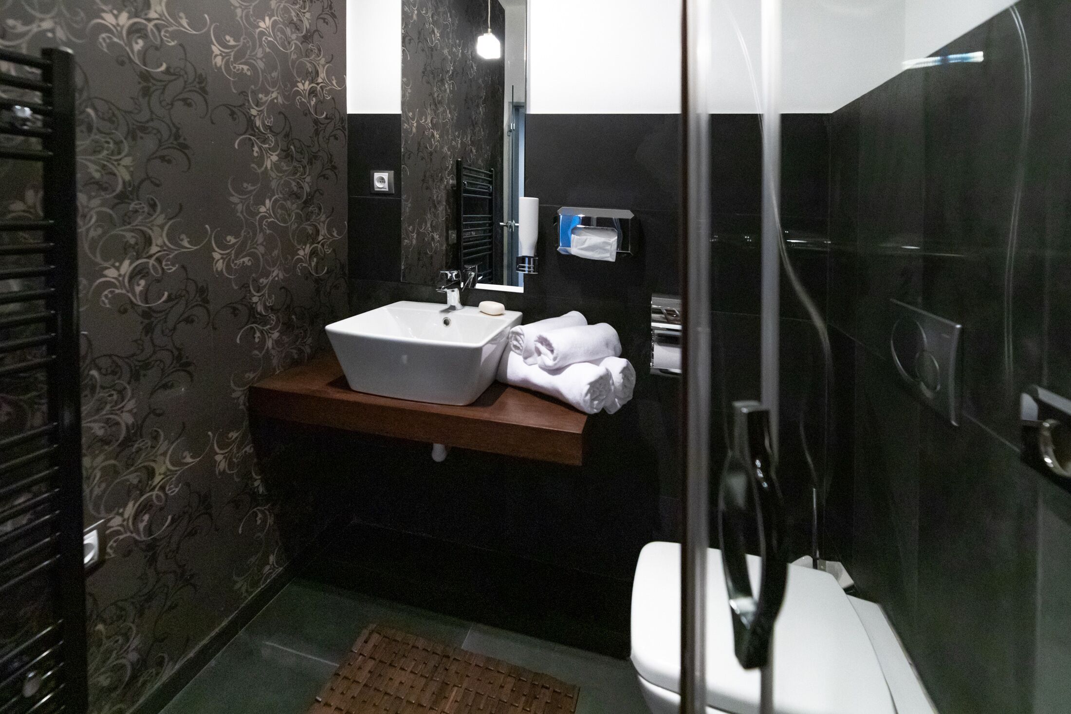 Un baño moderno con un lavamanos independiente, un perchero y un box de ducha de vidrio.