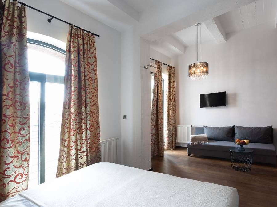 A modern bedroom with a large bed, a sofa, and a TV in a living area.