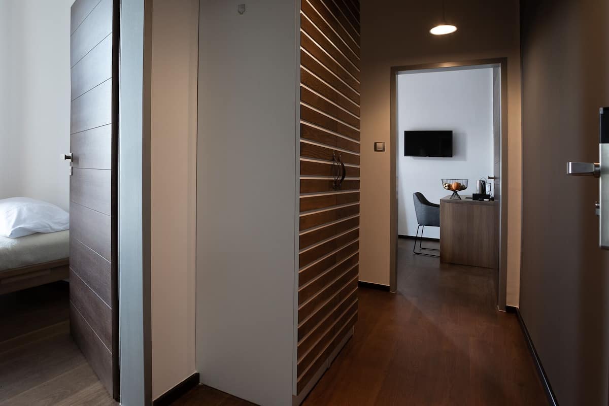 Quarto de hotel moderno com cama, parede de ripas de madeira, televisão e uma pequena cozinha.