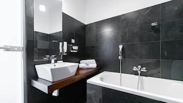 Un baño moderno con un lavamanos blanco, una bañera y paredes de azulejos oscuros.