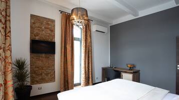 A modern hotel room with a large bed, a desk, a potted plant, and a TV mounted on a brick wall.