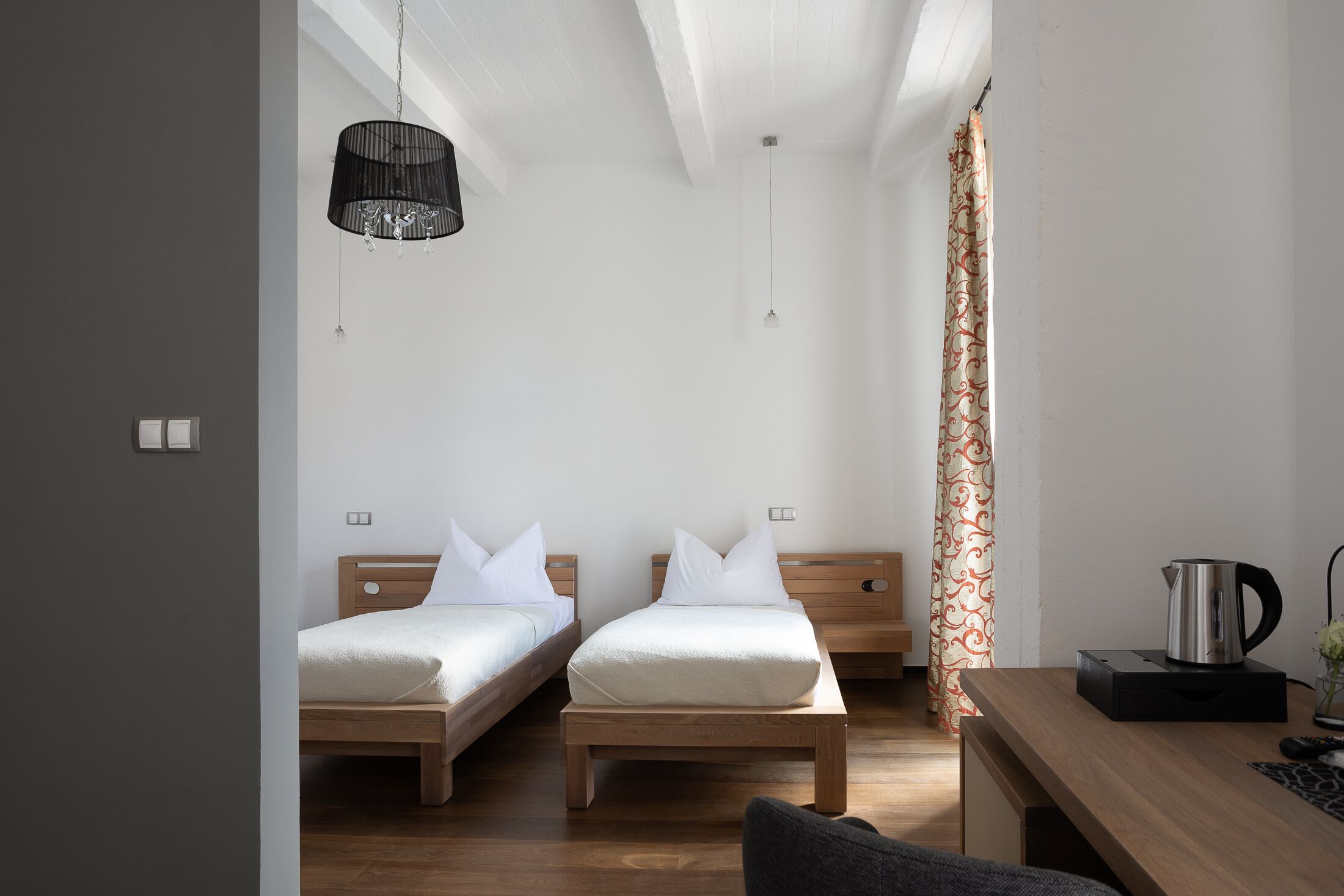 Quarto com duas camas de madeira, uma escrivaninha de madeira, um bule e um cortador com padrão.