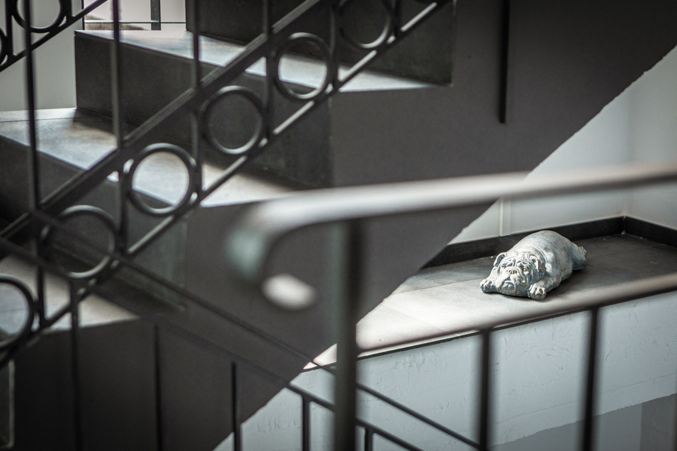 Eine Treppe mit Metallgeländer und einer Statue eines ruhenden Hundes auf der Podestfläche.