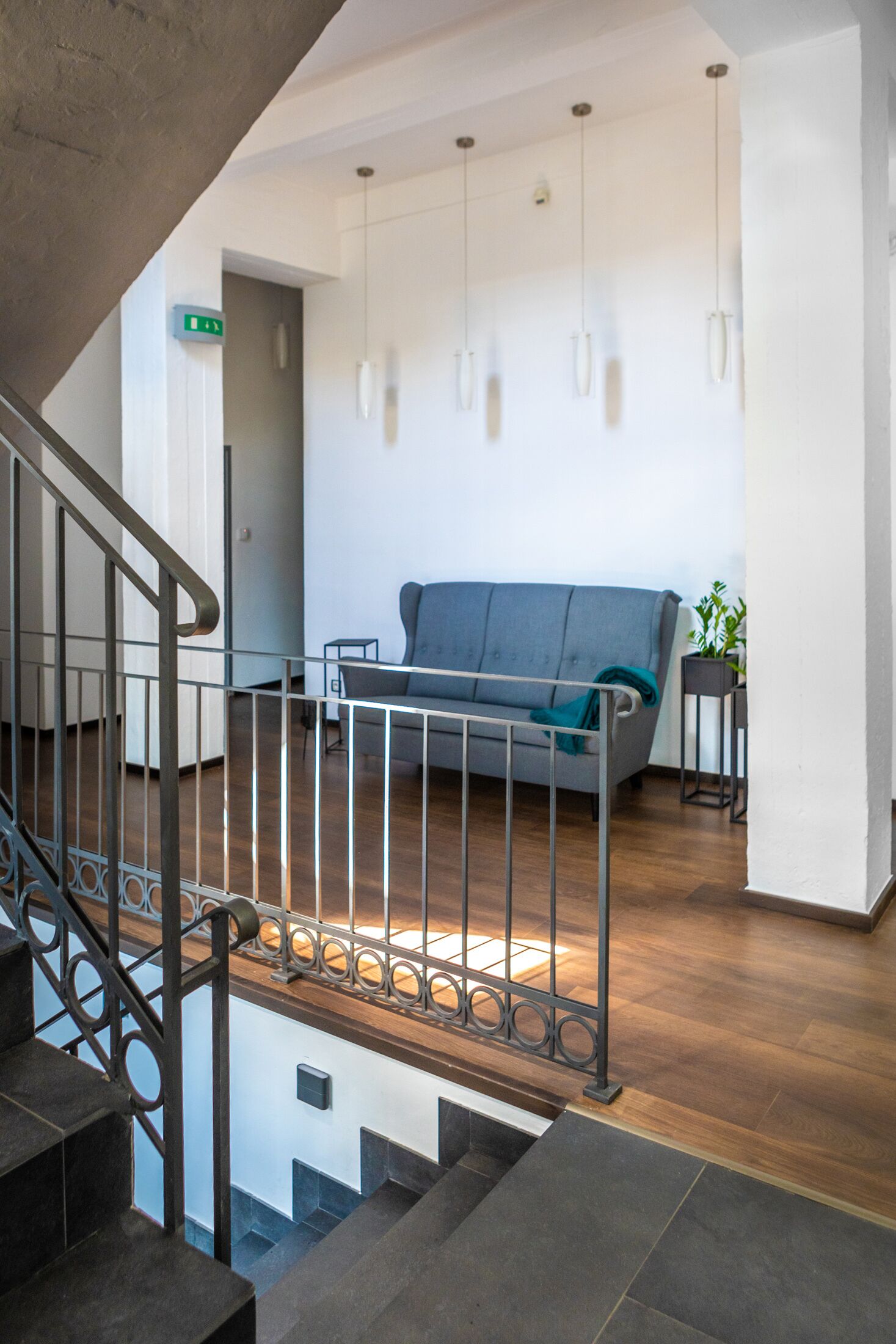 A modern interior with a staircase, a grey sofa, and hanging pendant lights.