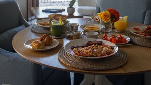 Une table de petit-déjeuner dressée avec des assiettes remplies de nourriture, un vase avec des fleurs et une fenêtre donnant sur un paysage verdoyant.