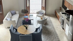 Un salon moderne comprenant un canapé, des fauteuils, une table basse et une table à manger. Il y a également un coin cuisine avec une cuisinière et des placards. La pièce est dotée d’une grande fenêtre offrant une vue sur l’extérieur.