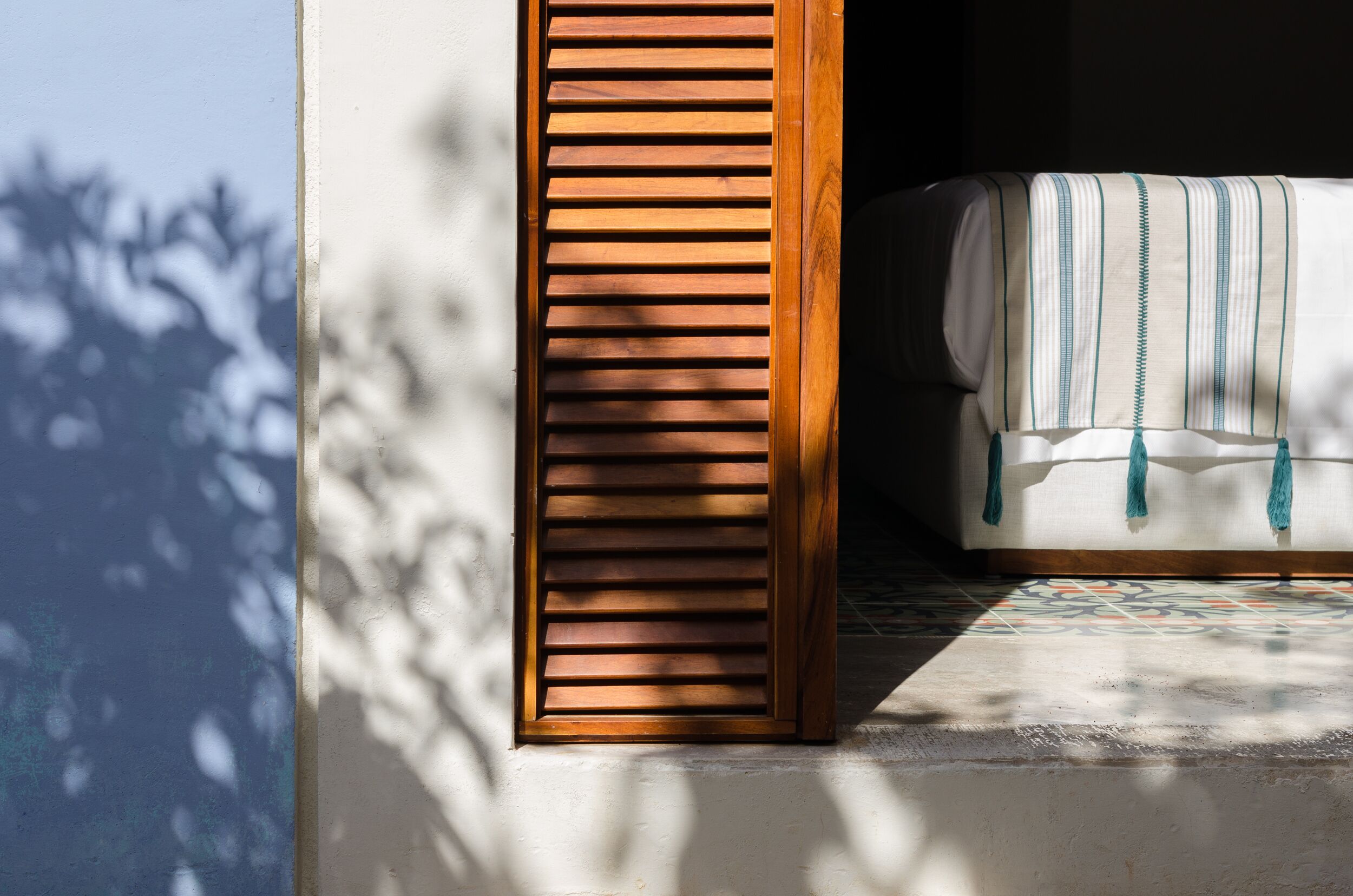 Ein Zimmer mit einem Fenster aus Holzlatten, einem gemusterten Boden und einem Bett mit einer Streifenoptik.