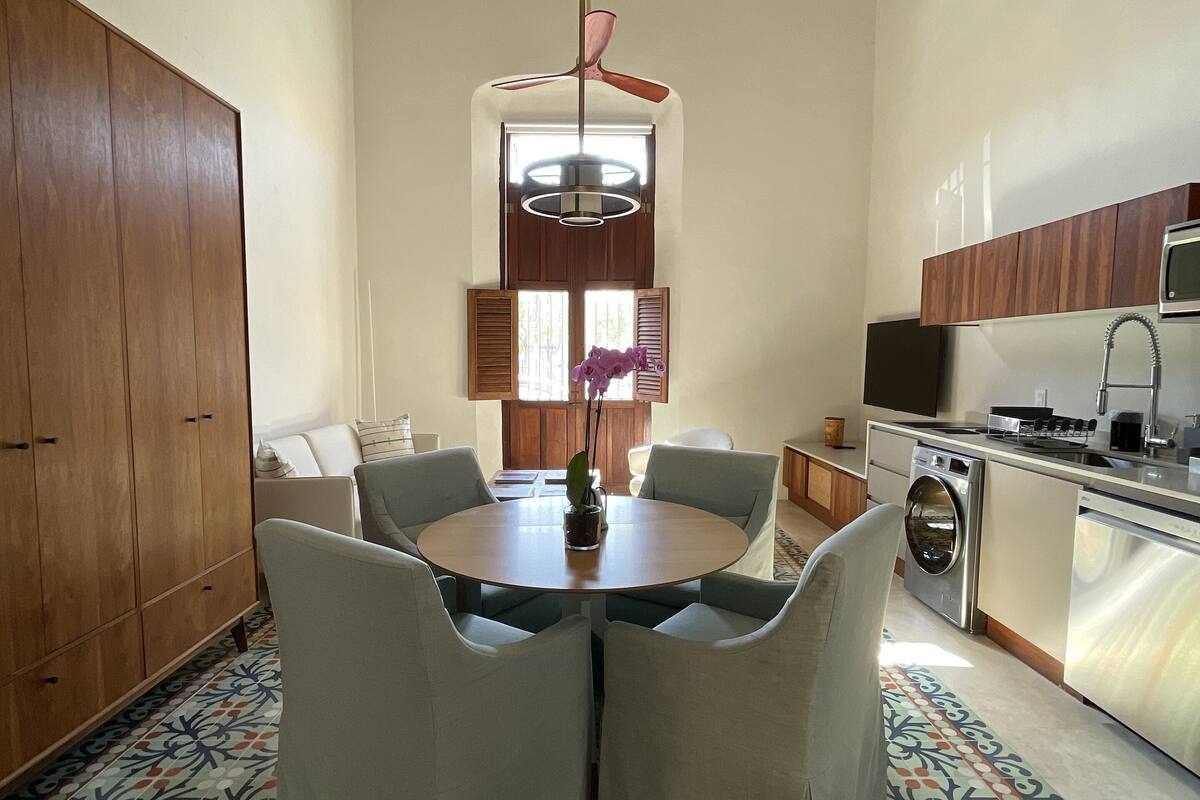 Una cocina moderna con horno empotrado, un fregadero y un microondas. Hay una zona de comedor con una mesa redonda y cuatro sillas.