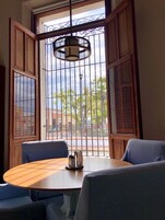 Una habitación con una mesa redonda, dos sillas, una lámpara colgante y vistas a través de una ventana con barrotes.