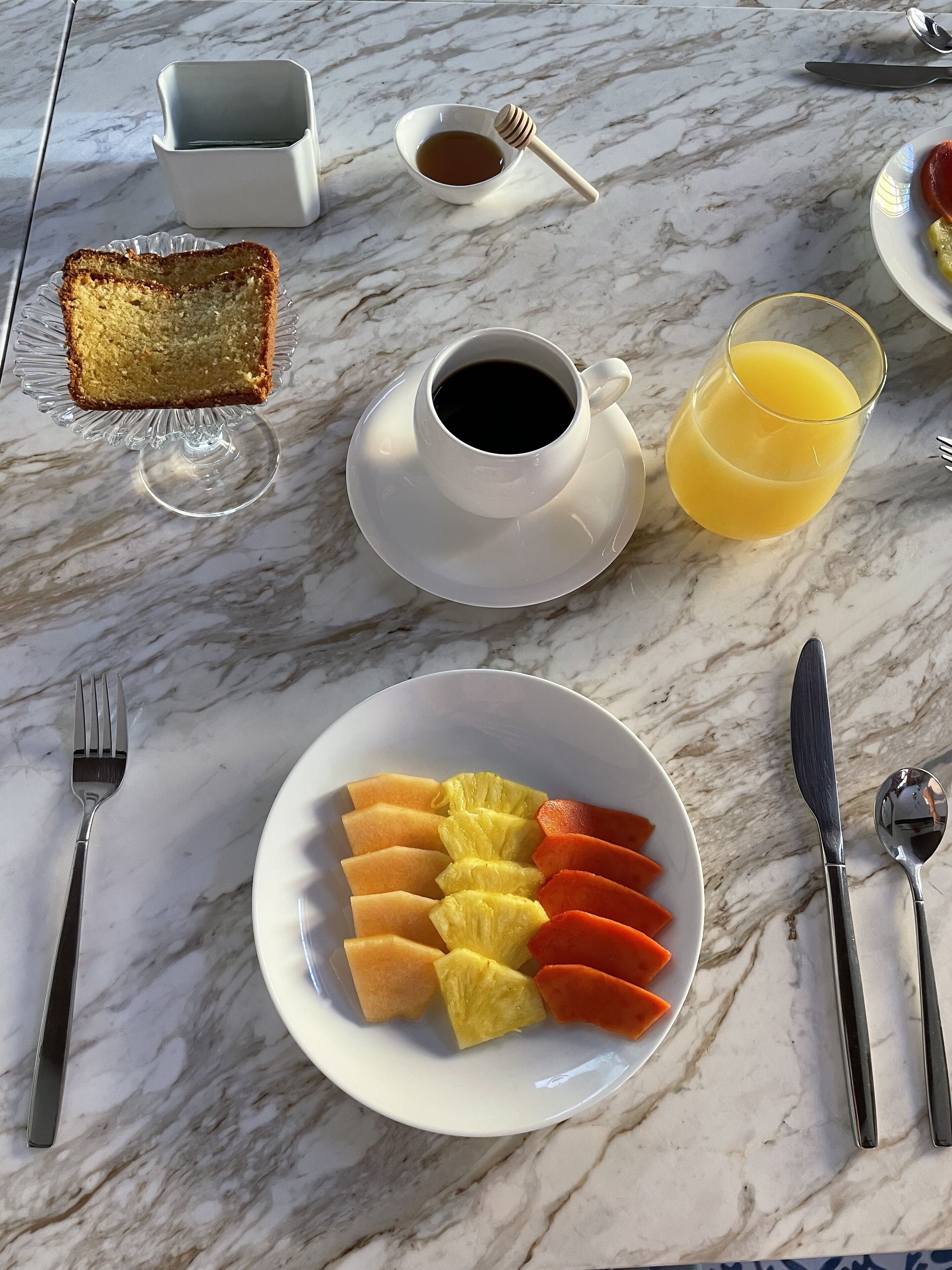 A breakfast setting with toast, coffee, orange juice, and fruit on a marble table.