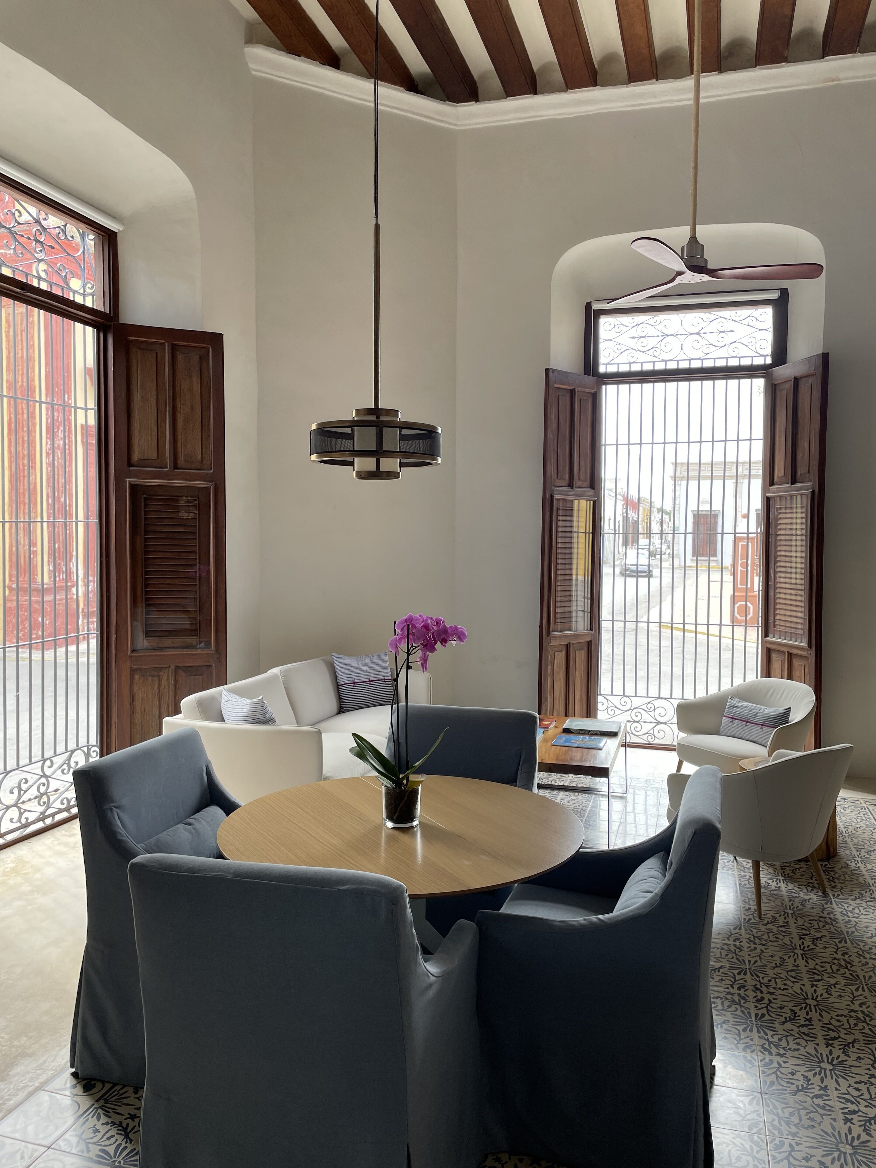A modern living room with a round wooden table, dark blue chairs, a white sofa, and a purple orchid in a glass vase.