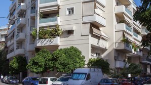 A multi-story residential building with balconies, parked cars, and a clear blue sky. - Great apt with amazing view in Koukaki (Athens)