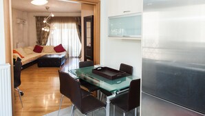 A modern living room with a glass dining table, dark chairs, a sofa with red cushions, and a large stainless steel refrigerator. - Great apt with amazing view in Koukaki (Athens)