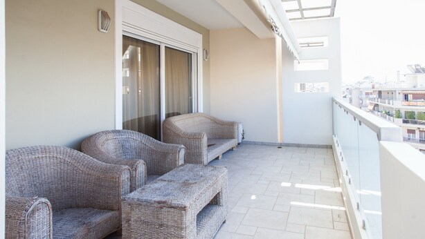 A balcony with wicker furniture, a sliding glass door, and a view of the cityscape. - Great apt with amazing view in Koukaki (Athens)