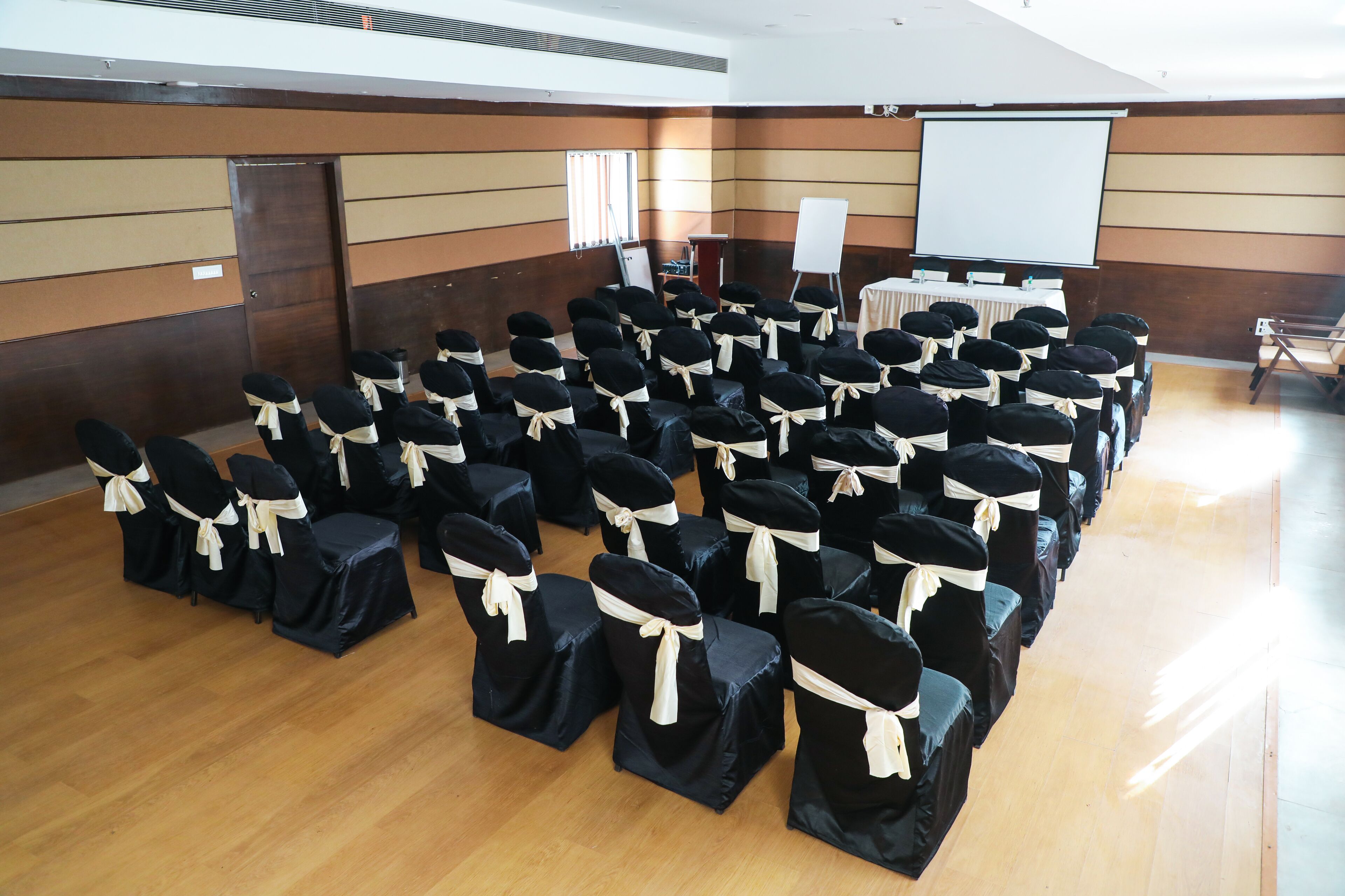 Une salle de conférence avec des rangées de chaises, un pupitre, un écran de projection et un tableau blanc.
