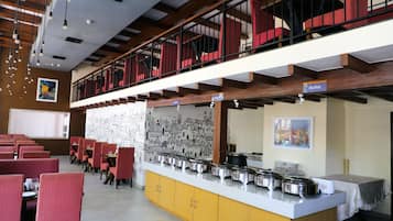 A buffet area with multiple serving stations, a counter with food containers, and a seating area with red chairs.
