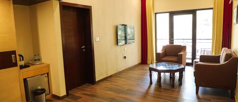 A room with a wooden floor, a sofa, a coffee table, a small table with a trash bin, a refrigerator, and a door.